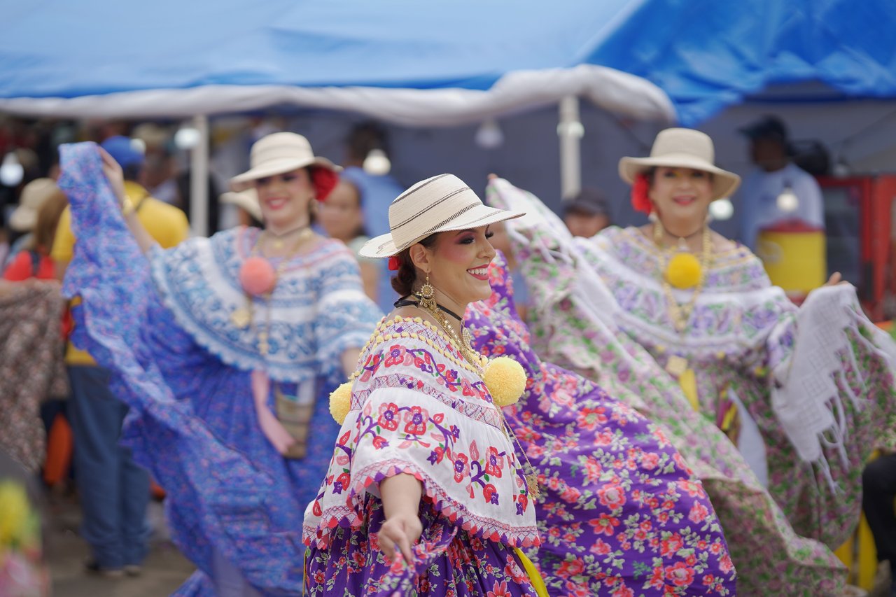 Panamanian women in traditional Pollera dresses dance joyously at a cultural festival.