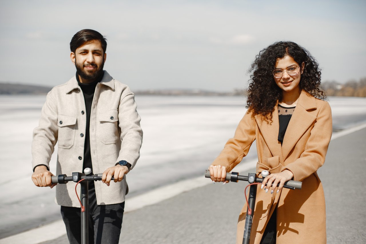 Happy couple riding e-scooters along scenic path on a bright day, embracing leisure and togetherness.