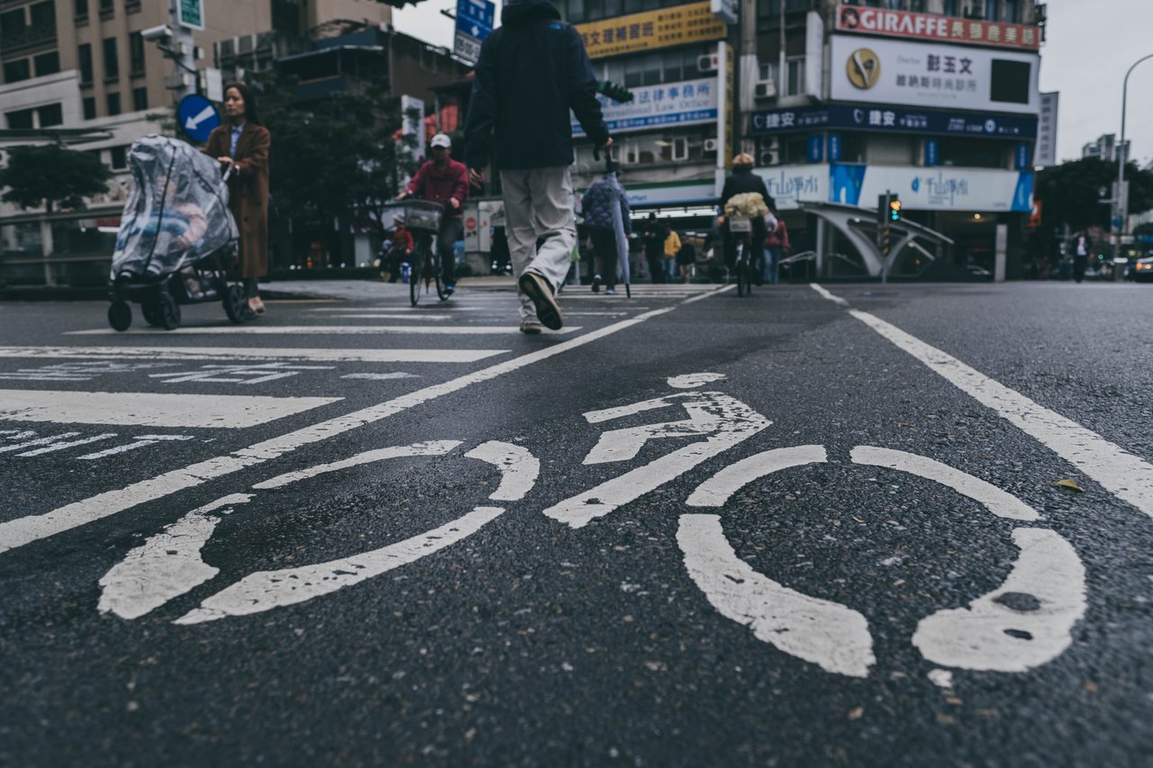 Busy urban street scene in Taiwan with bicycle lane markings and pedestrians crossing.