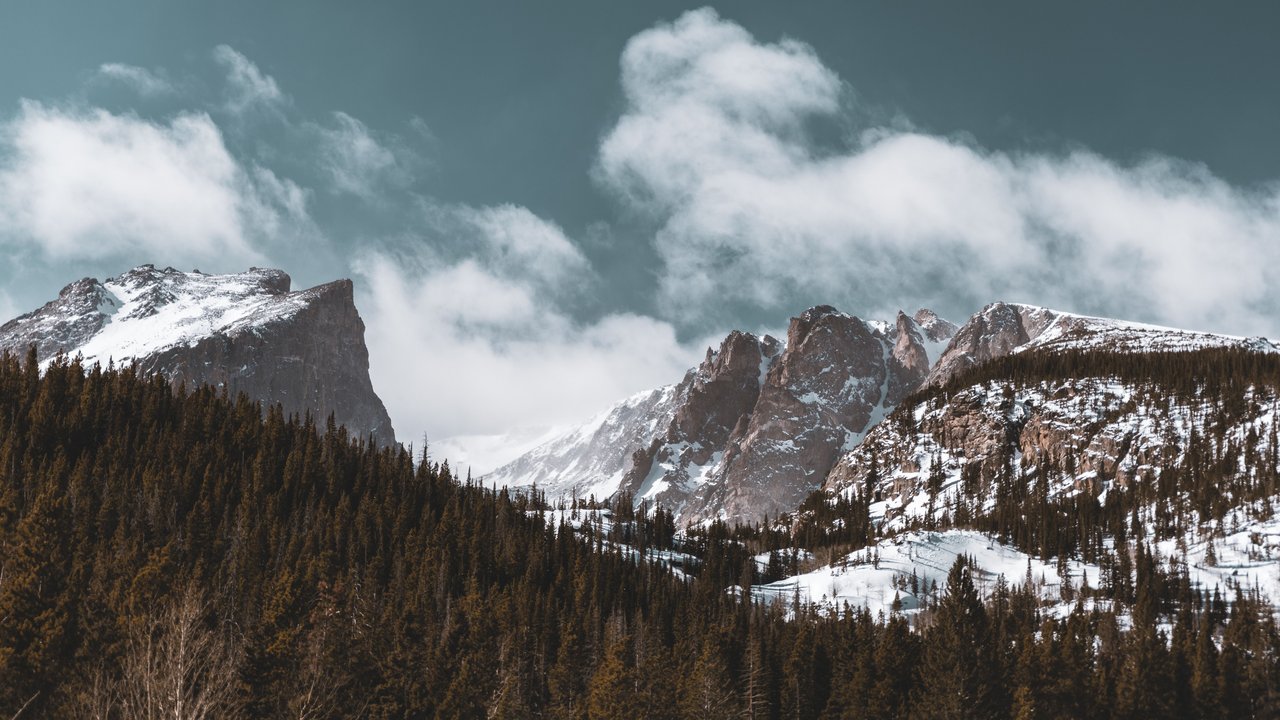 Snow-covered mountains and pine trees under a cloudy sky in Colorado's winter landscape.