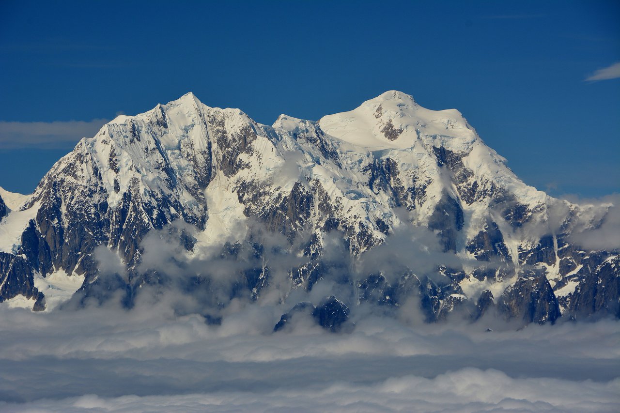 Stunning view of snow-capped mountains in Alaska, surrounded by clouds and blue skies.