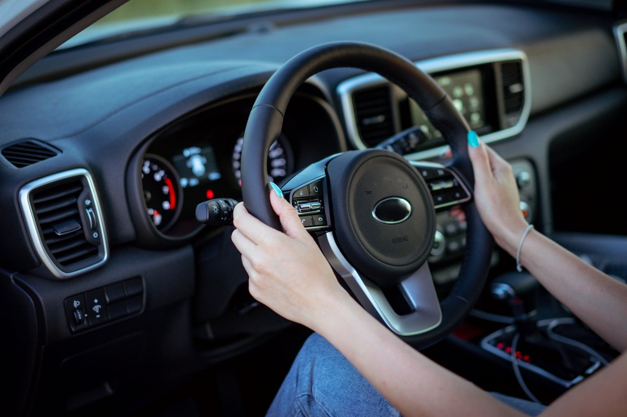 Close-up of a woman's hands on a steering wheel in a modern car interior.