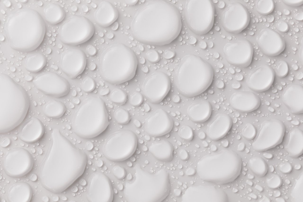 Closeup top view of white plain even surface with many abstract still glassy liquid drops of different shapes and sizes