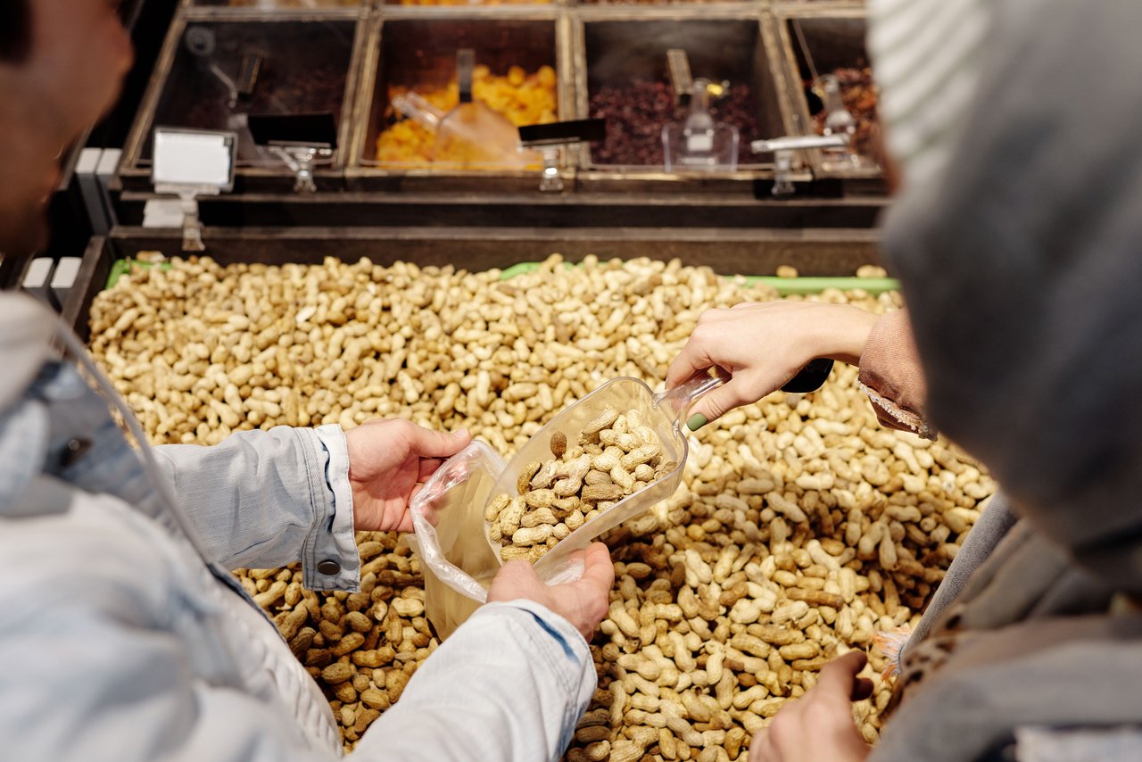 Two people buying peanuts in a supermarket using a scoop. Fresh and bulk food concept.