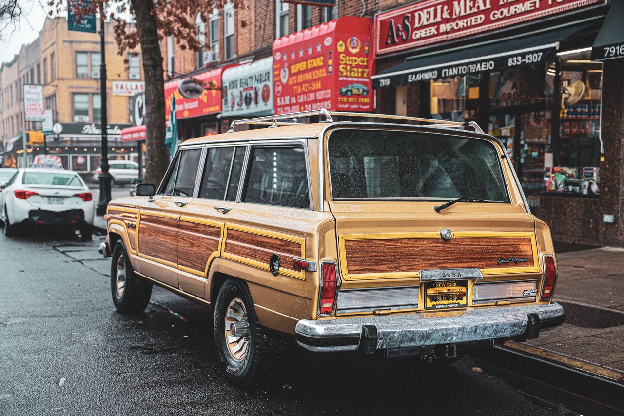 Classic vintage Wagoneer parked on a bustling city street with storefronts and urban vibe.