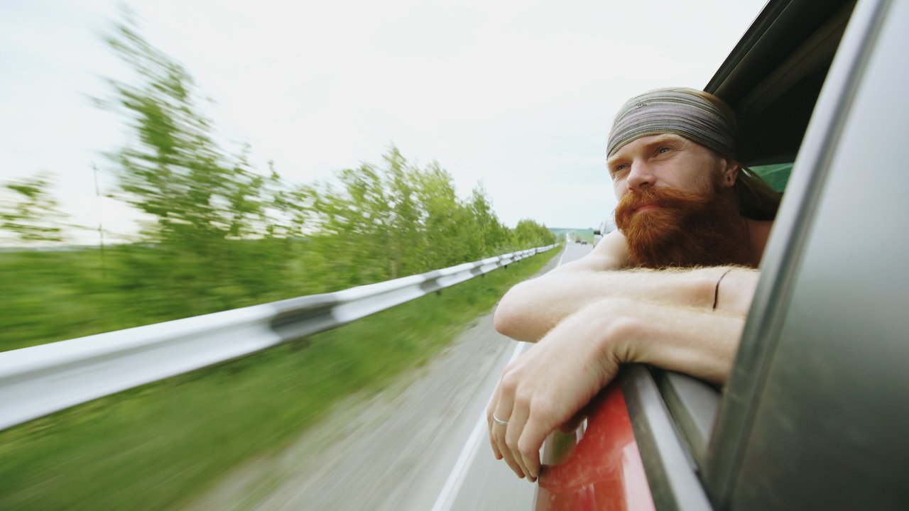 A man leans out to enjoy the view, his beard and relaxed pose reflecting the joy of a scenic road trip.