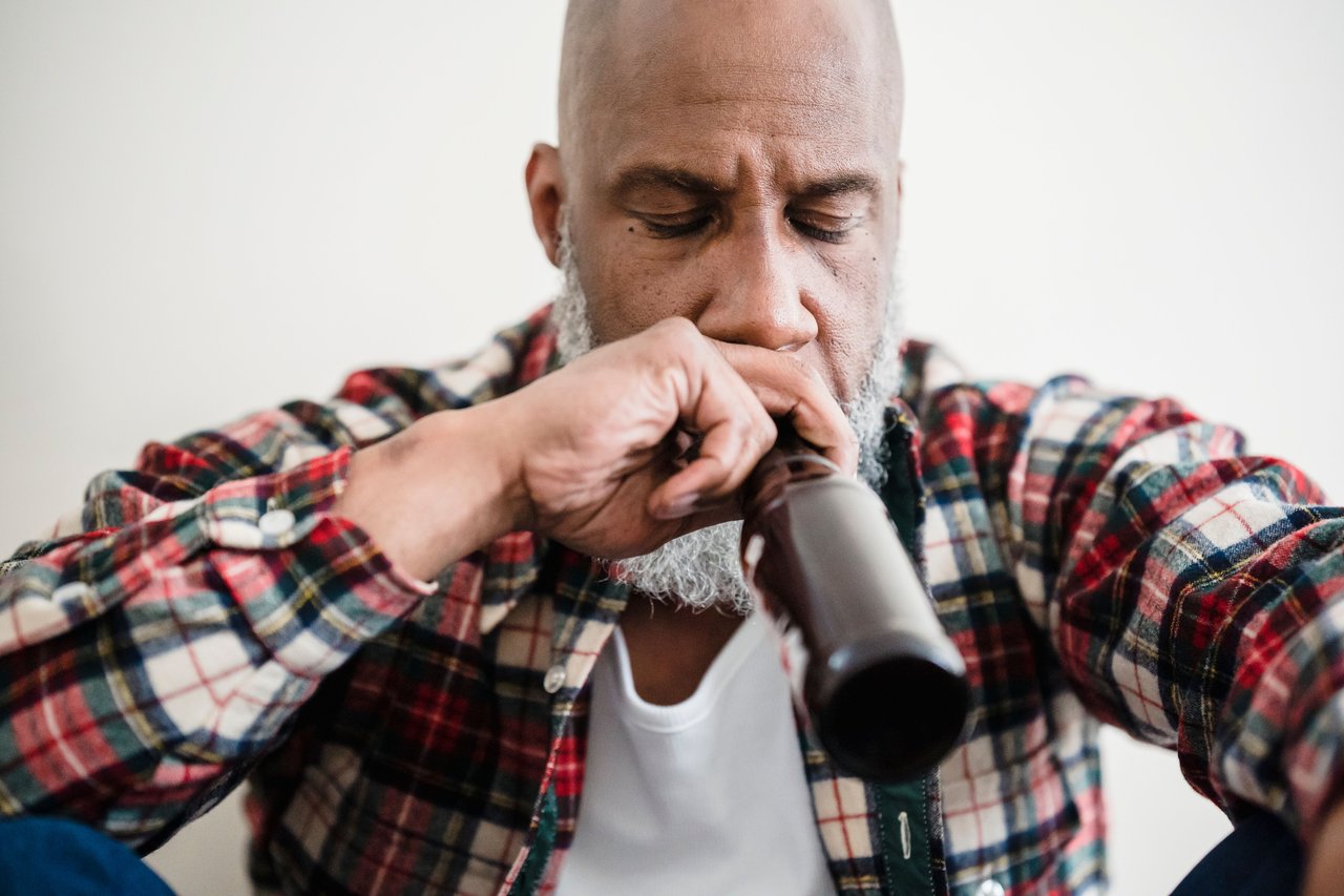 Adult man sitting indoors looking pensive with a beer bottle, conveying emotions of stress or contemplation.