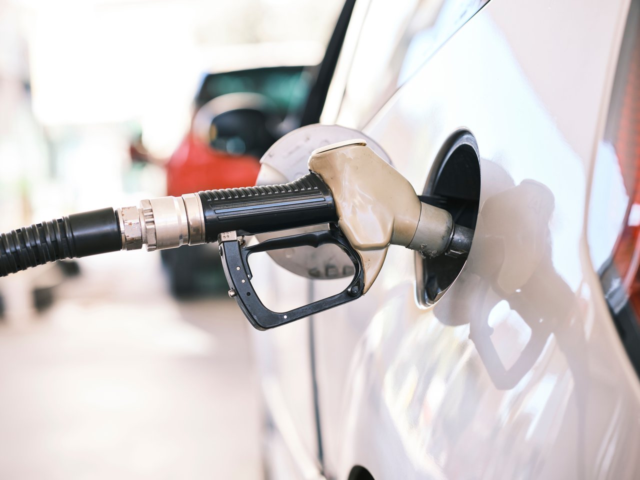Fuel nozzle inserted in car at a gas station, close-up view emphasizing energy and transportation themes.