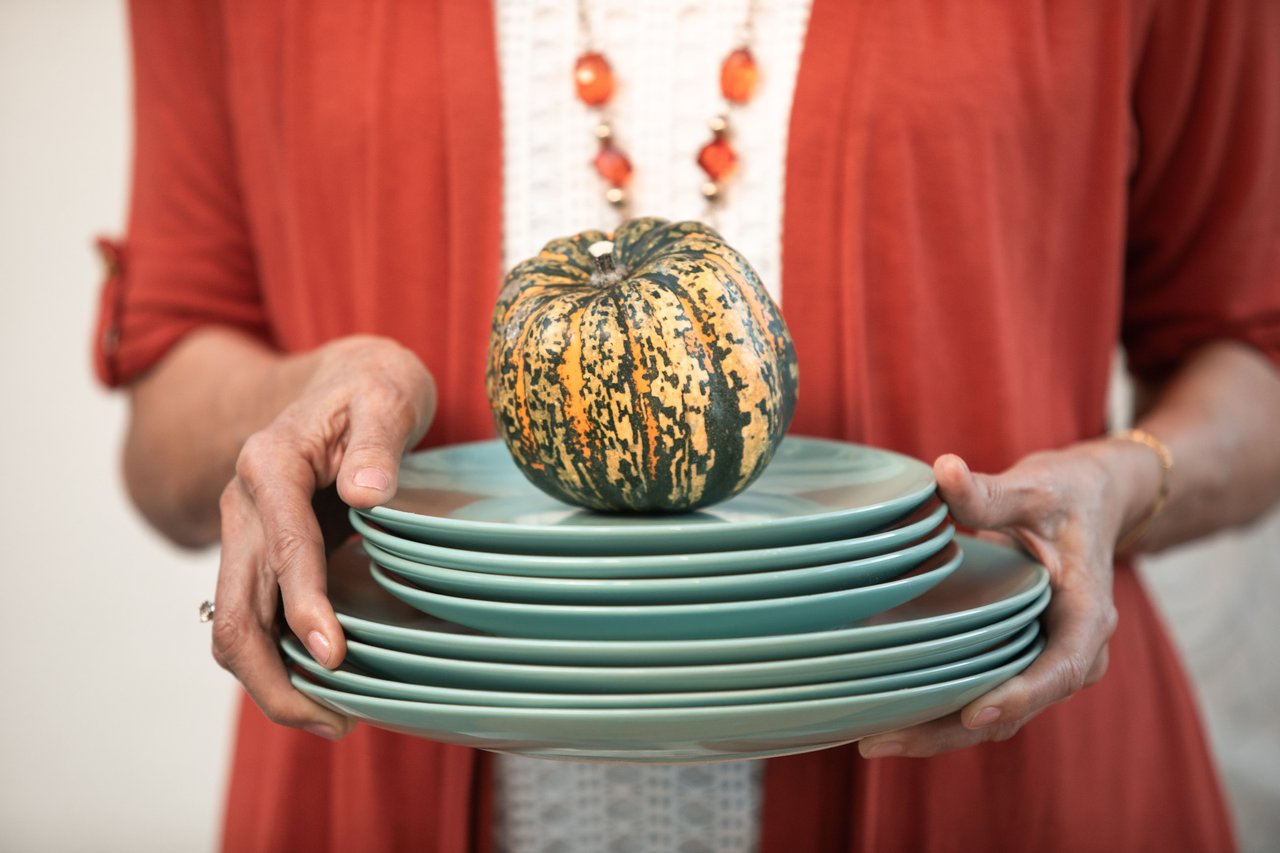 Close-up of woman holding stacked plates with a decorative pumpkin, perfect for a fall holiday setting.