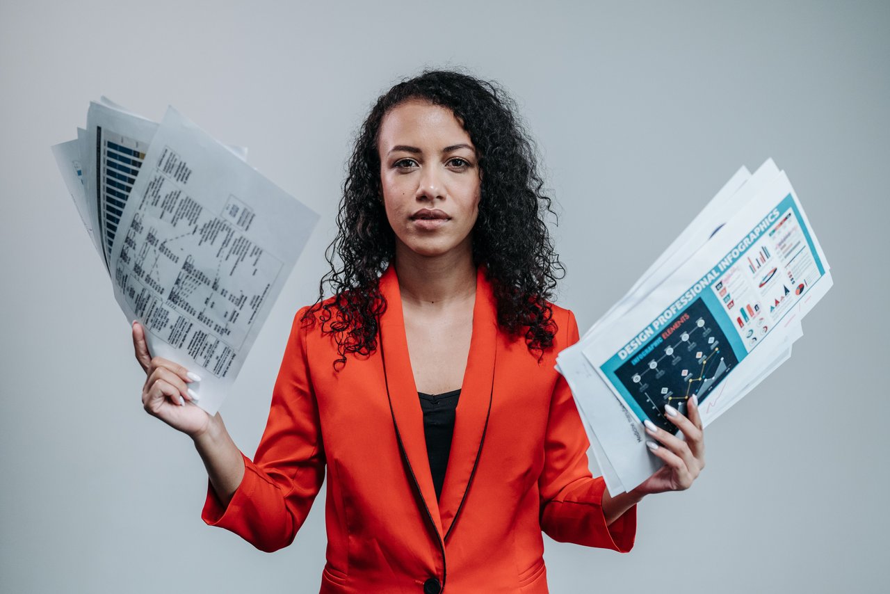 Businesswoman in red blazer holding analytical charts and infographics indoors.