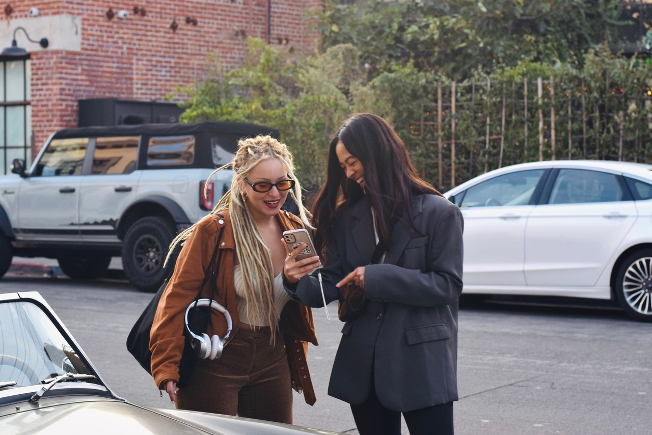 Two friends laughing and looking at a smartphone on a city street in Los Angeles.