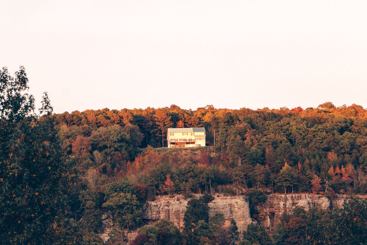 A secluded house sits atop a cliff surrounded by vibrant autumn foliage in Arkansas.