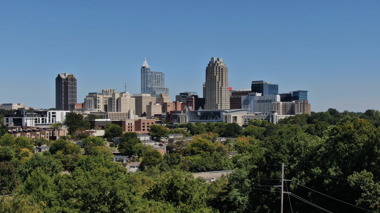 Raleigh, NC skyline featuring modern architecture and lush greenery on a clear day.